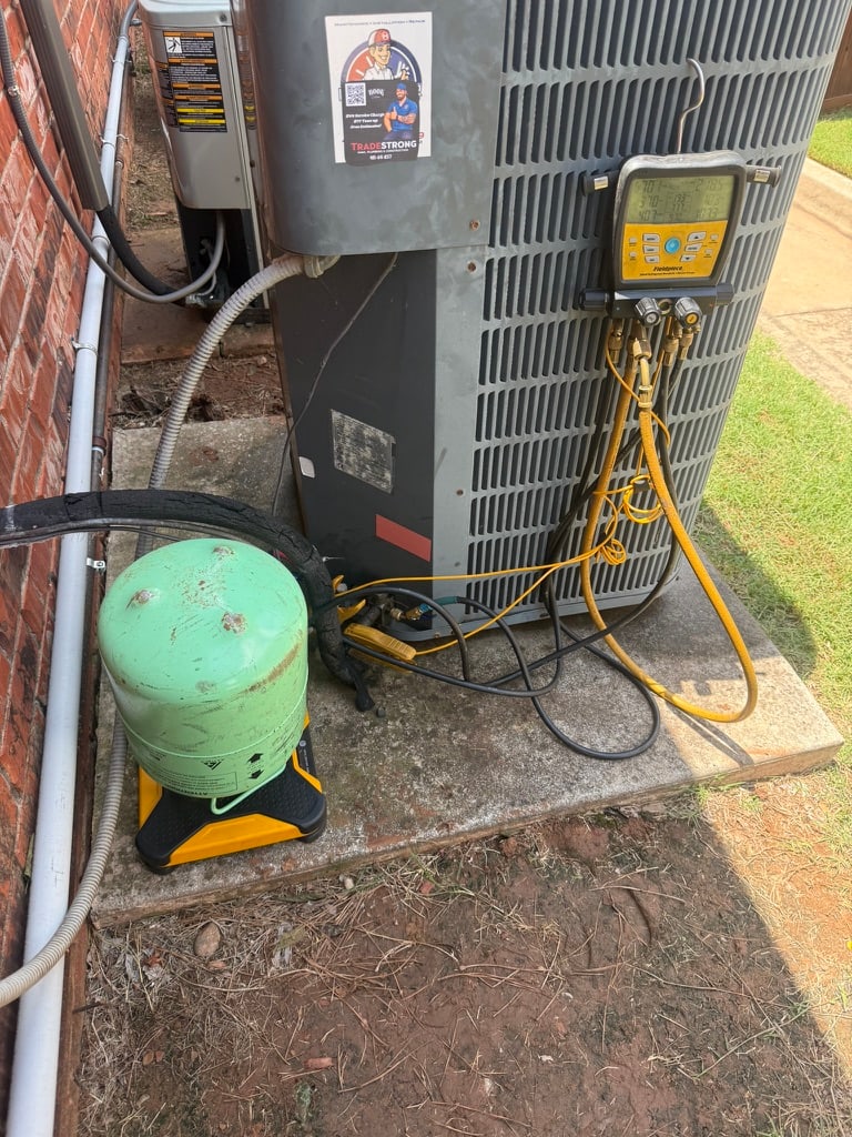 R-22 refrigerant cylinder and digital gauges connected to an older Norman air conditioner during TradeStrong HVAC service