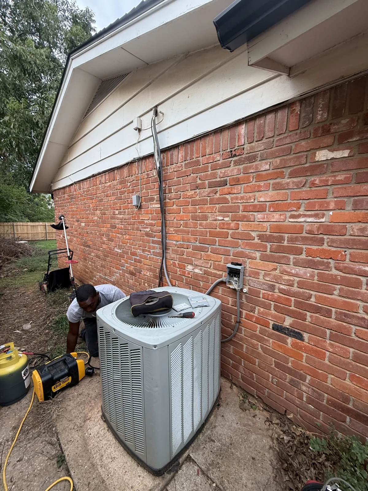 Existing outdoor air conditioner with a TradeStrong technician working beside it in Edmond