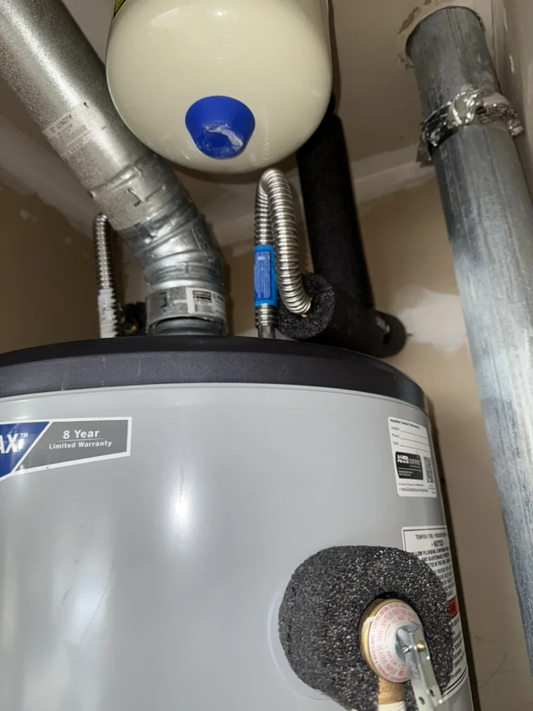 Close-up of the new water heater showing its 8-year limited warranty label, top connections, and expansion tank