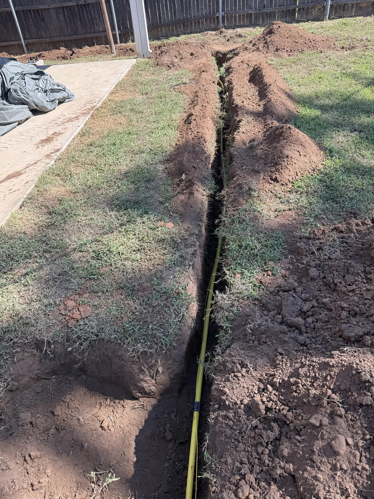 New yellow gas service piping in a trench crossing the backyard beside the patio
