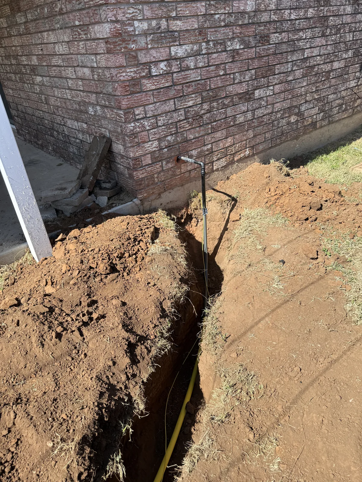 Gas service riser emerging from the trench at the corner of the brick house