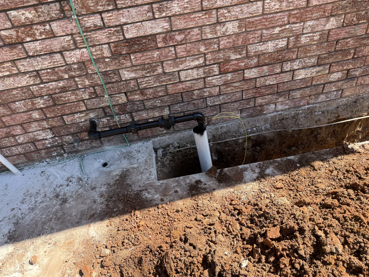 New above-ground gas piping and riser at the brick wall beside the excavated patio