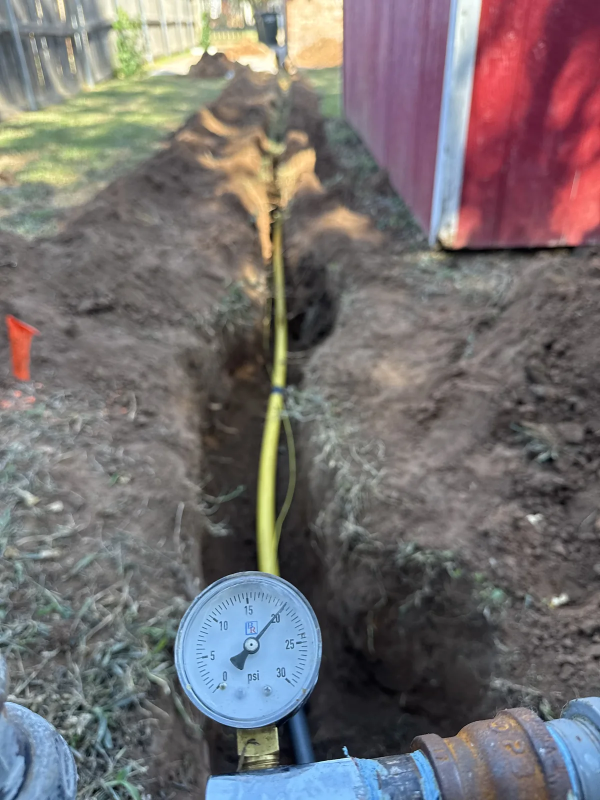 Pressure-test gauge in the foreground with new gas piping in the trench behind it