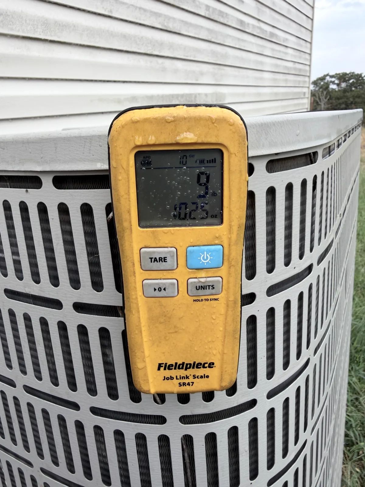 Fieldpiece refrigerant scale display hanging on the outdoor condenser